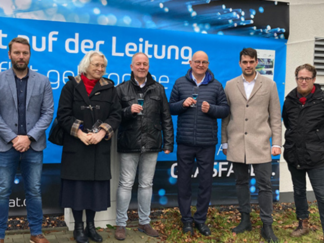 Sechs Personen stehen vor einem Banner von Komflat