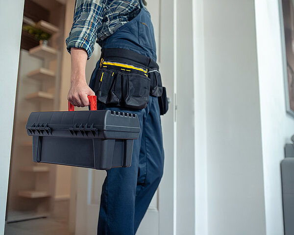 Mann in Arbeitsbekleidung mit Werkzeugkoffer geht durch eine Tür