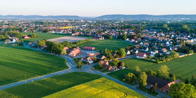 Luftaufnahme mit Wohnhäusern und umliegenden Feldern bei sonnigem Wetter.
