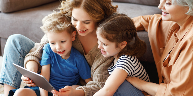 Frau sitzt mit zwei Kindern und einer älteren Person auf dem Sofa