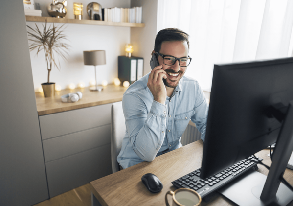 Mann sitzt am PC mit Telefon in der Hand