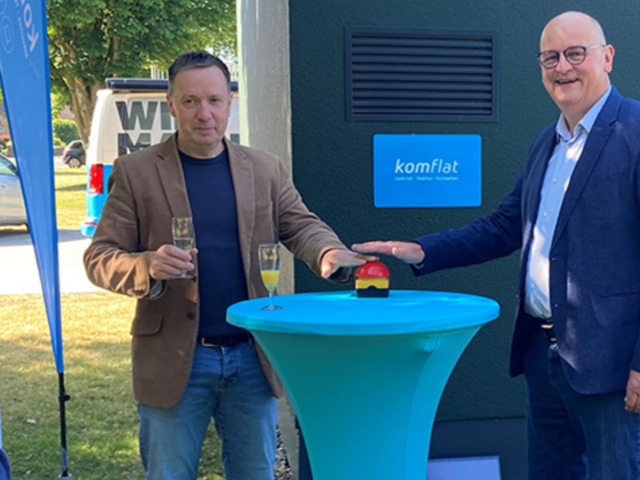 Zwei Personen drücken gemeinsam auf einen großen roten Knopf