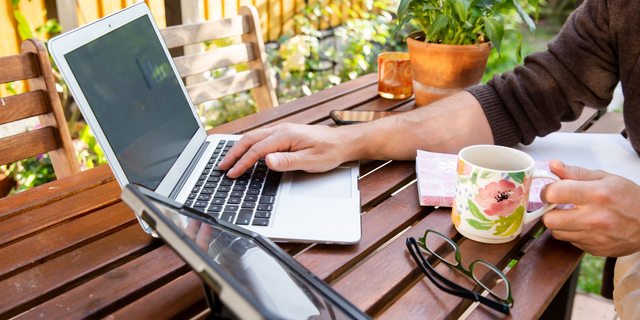 Person arbeitet draußen am Holztisch mit einem Laptop