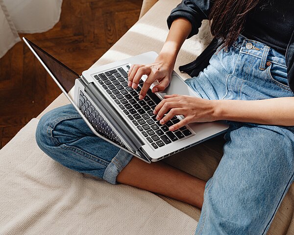 Person sitzt im Schneidersitz auf einem Sofa