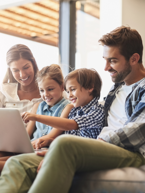 Eine Familie sitzt zusammen auf der Couch und sieht gemeinsam auf einen Laptop