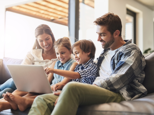 Eine Familie sitzt zusammen auf der Couch und sieht gemeinsam auf einen Laptop