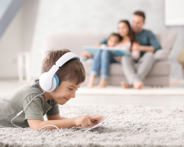 Ein kleiner Junge liegt auf dem Teppich im Wohnzimmer und spielt fröhlich mit seinem Tablet