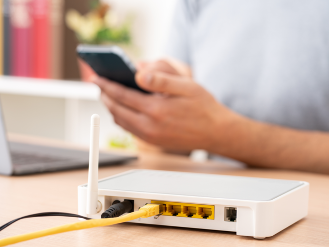 Router im Vordergrund, Hand mit Handy im Hintergrund