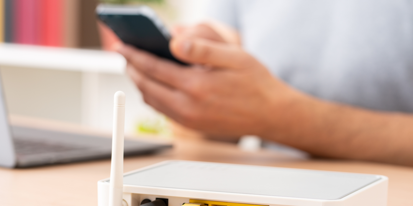 Router im Vordergrund, Hand mit Handy im Hintergrund Router im Vordergrund, Hand mit Handy im Hintergrund