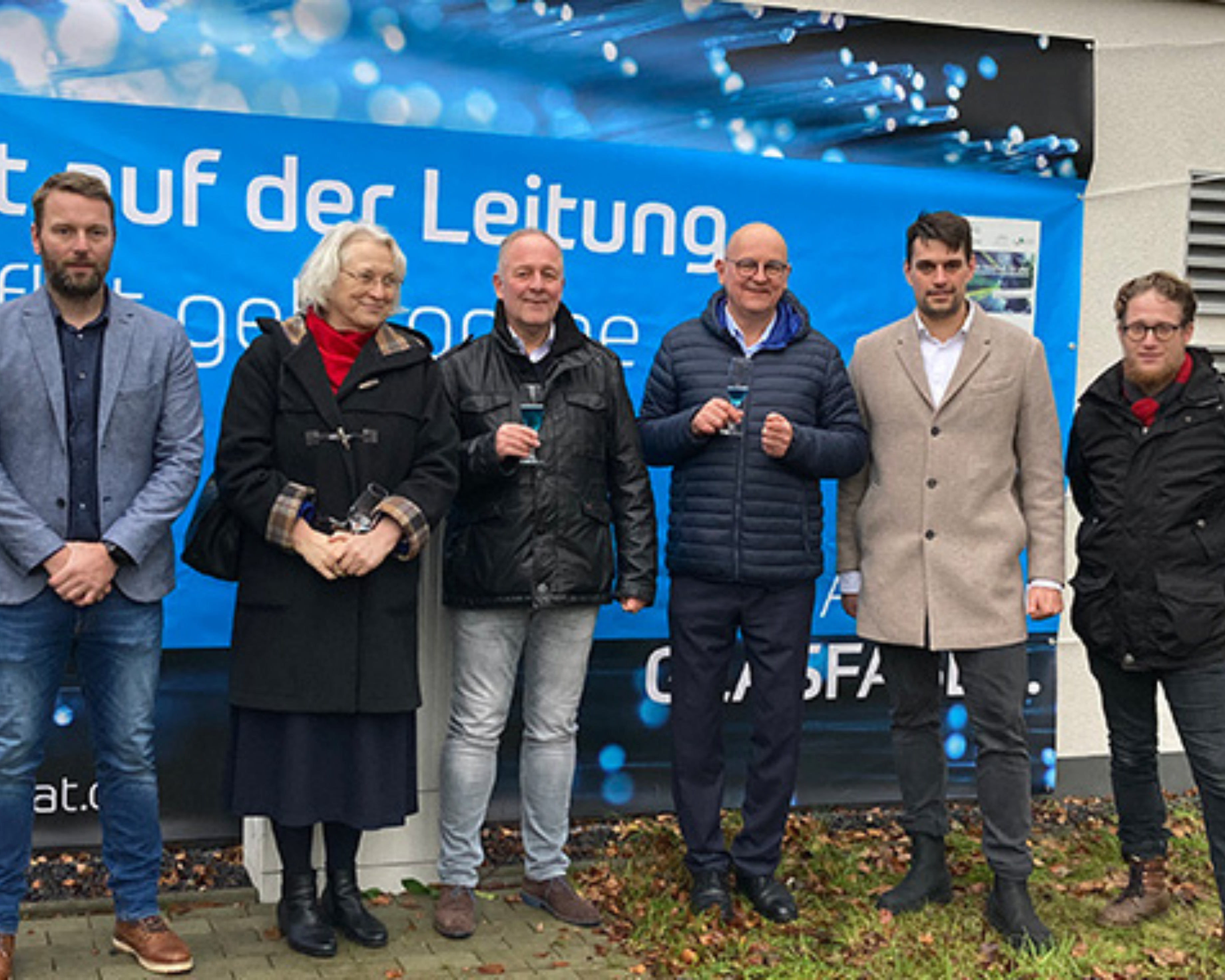 Sechs Personen stehen vor einem Banner von Komflat