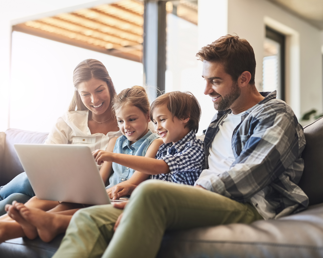 Eine Familie sitzt zusammen auf der Couch und sieht gemeinsam auf einen Laptop
